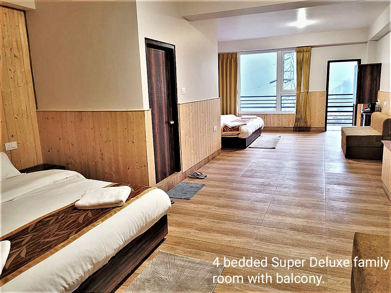 Family room with two double beds along a long pine-panelled room and a balcony door at the far end