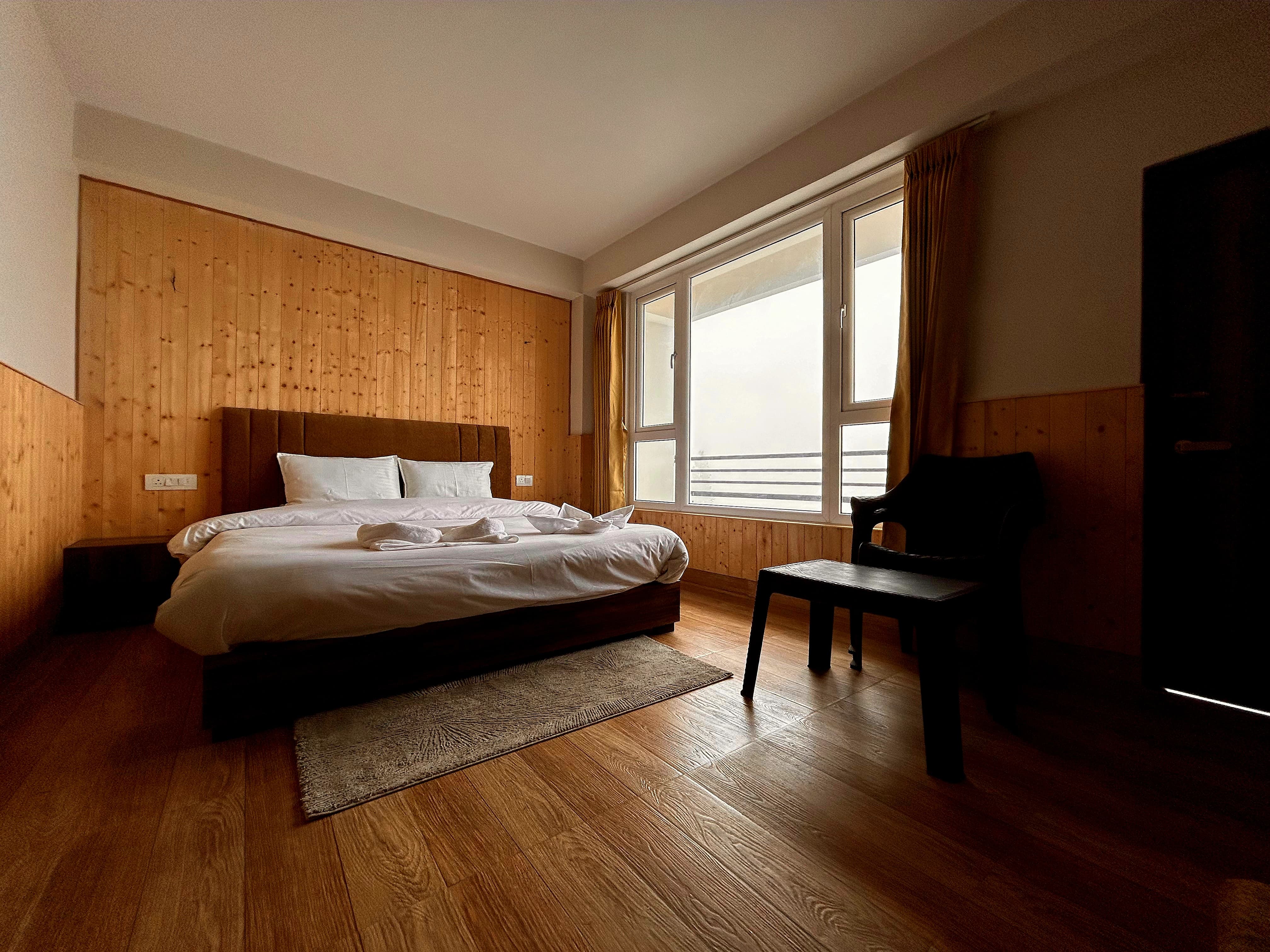 Double bed against a pine-panelled wall beside a wide window opening onto the balcony rail
